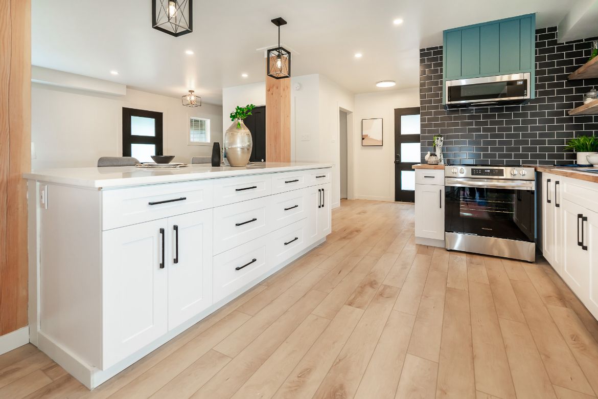 Kitchen with white cabinetry, a large island and dark tile backsplash